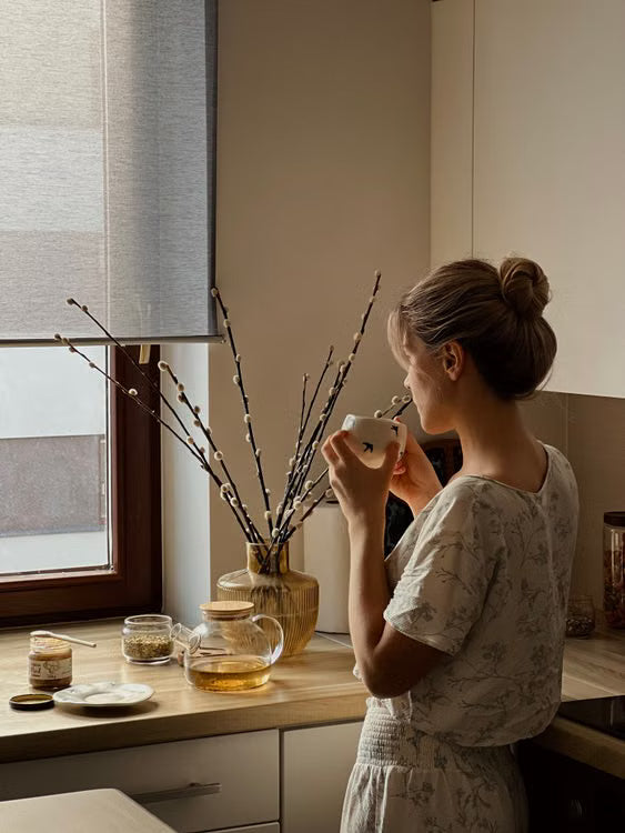Femme tenant une tasse de thé près d'une fenêtre, lumière du matin, moment de calme