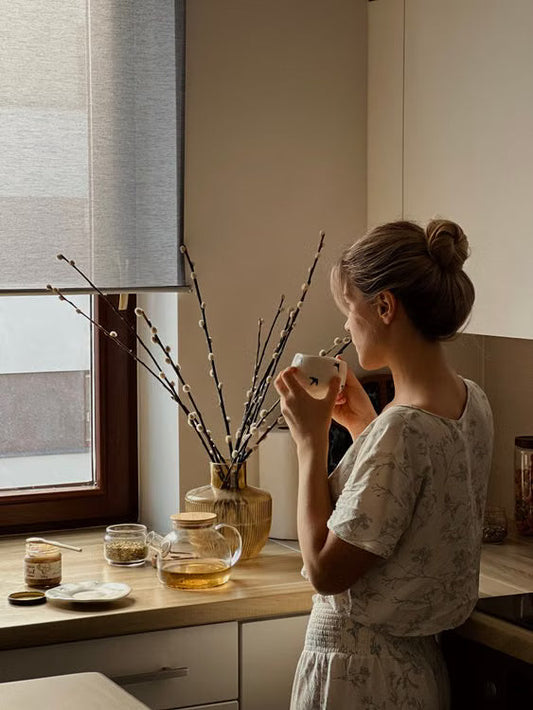 Femme tenant une tasse de thé près d'une fenêtre, lumière du matin, moment de calme