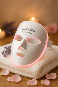 Masque LED LumiSpa Harmonie posé sur fond rosé avec serviettes et bougie